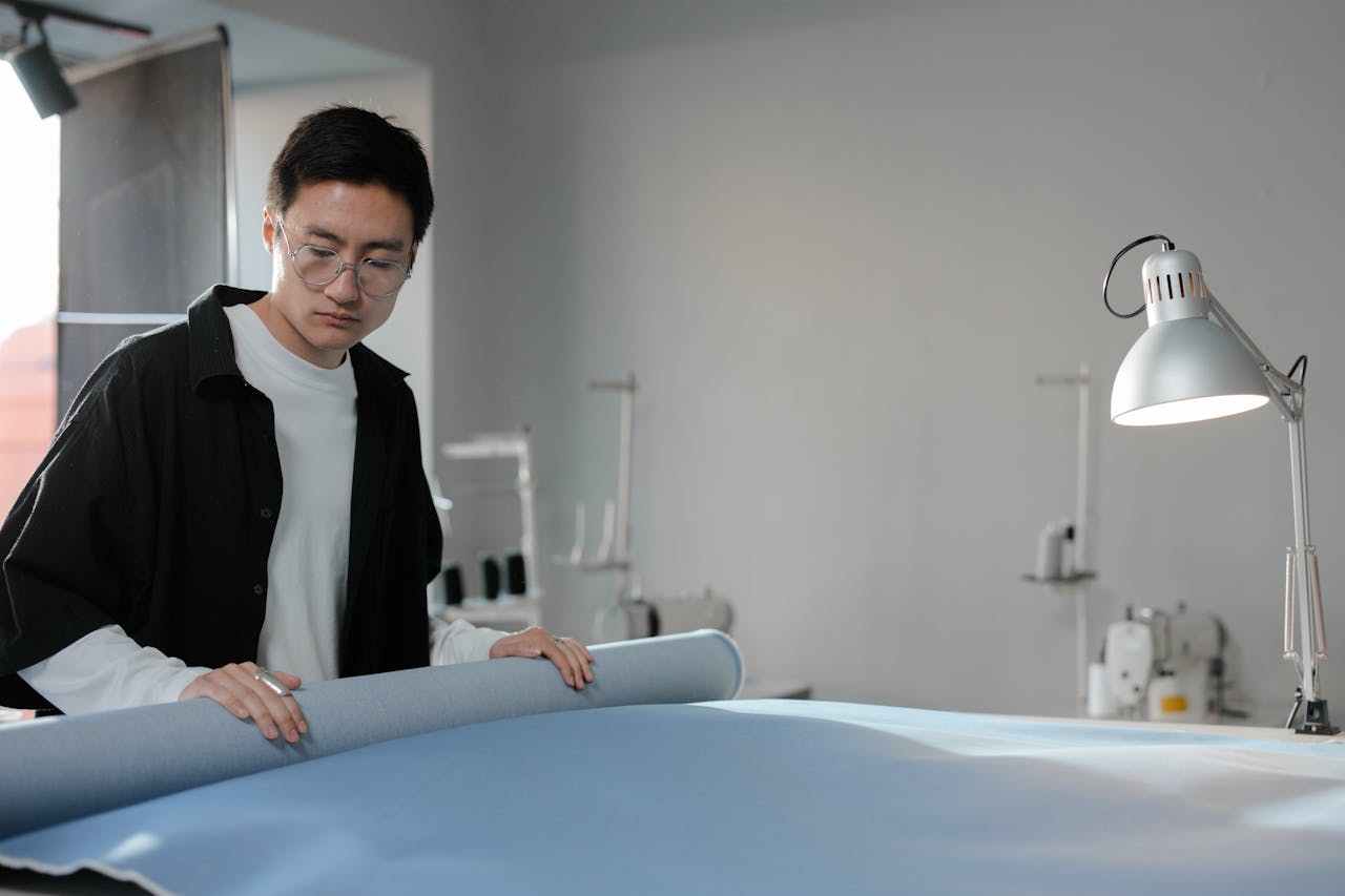 services-03 Fashion designer examining a blue fabric roll in a well-lit workspace.