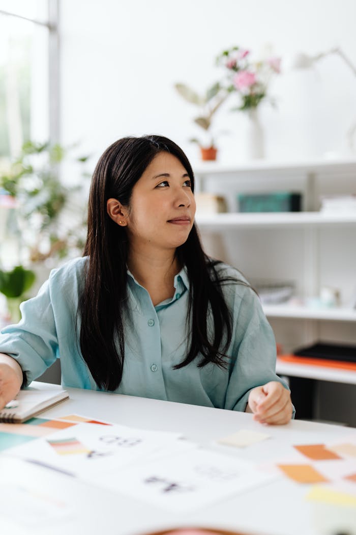 services-02 Asian woman seated in a bright office environment looking thoughtful while examining design swatches.